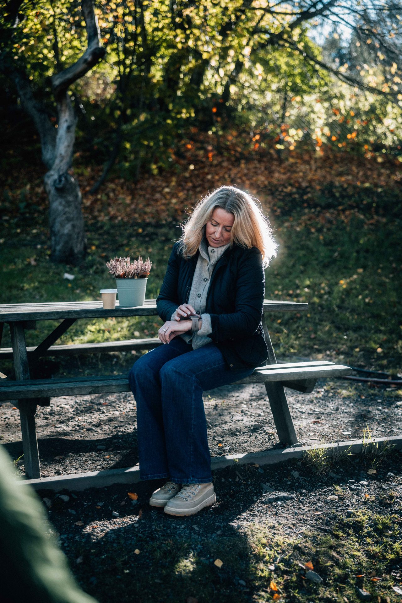 Woman in autumn setting checking her smartwatch on a wooden picnic bench.