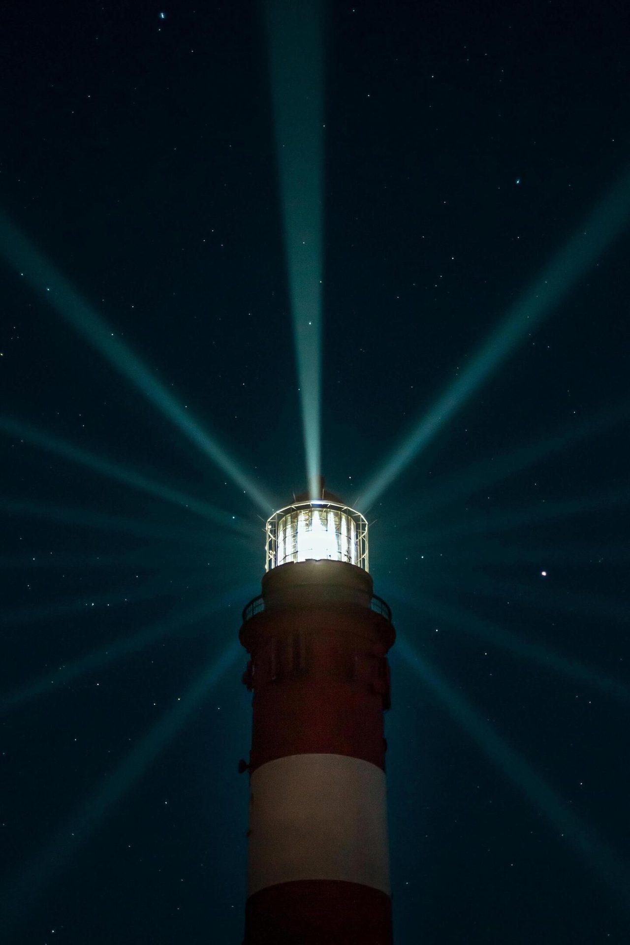 Bright lighthouse at night, its beams radiating into a dark, starry sky.