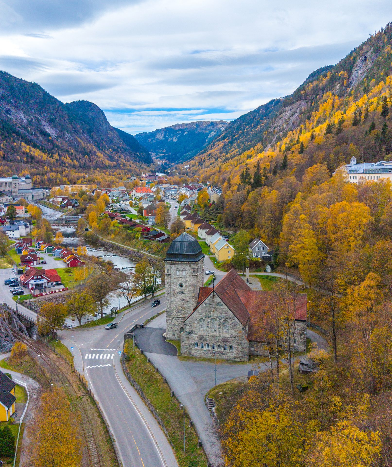 Aerial view of an autumn valley town with a stone church, river, and golden trees.