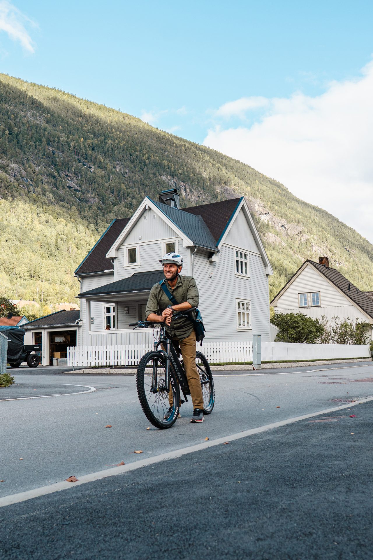 Smiling man on bike in a village with a mountain backdrop.