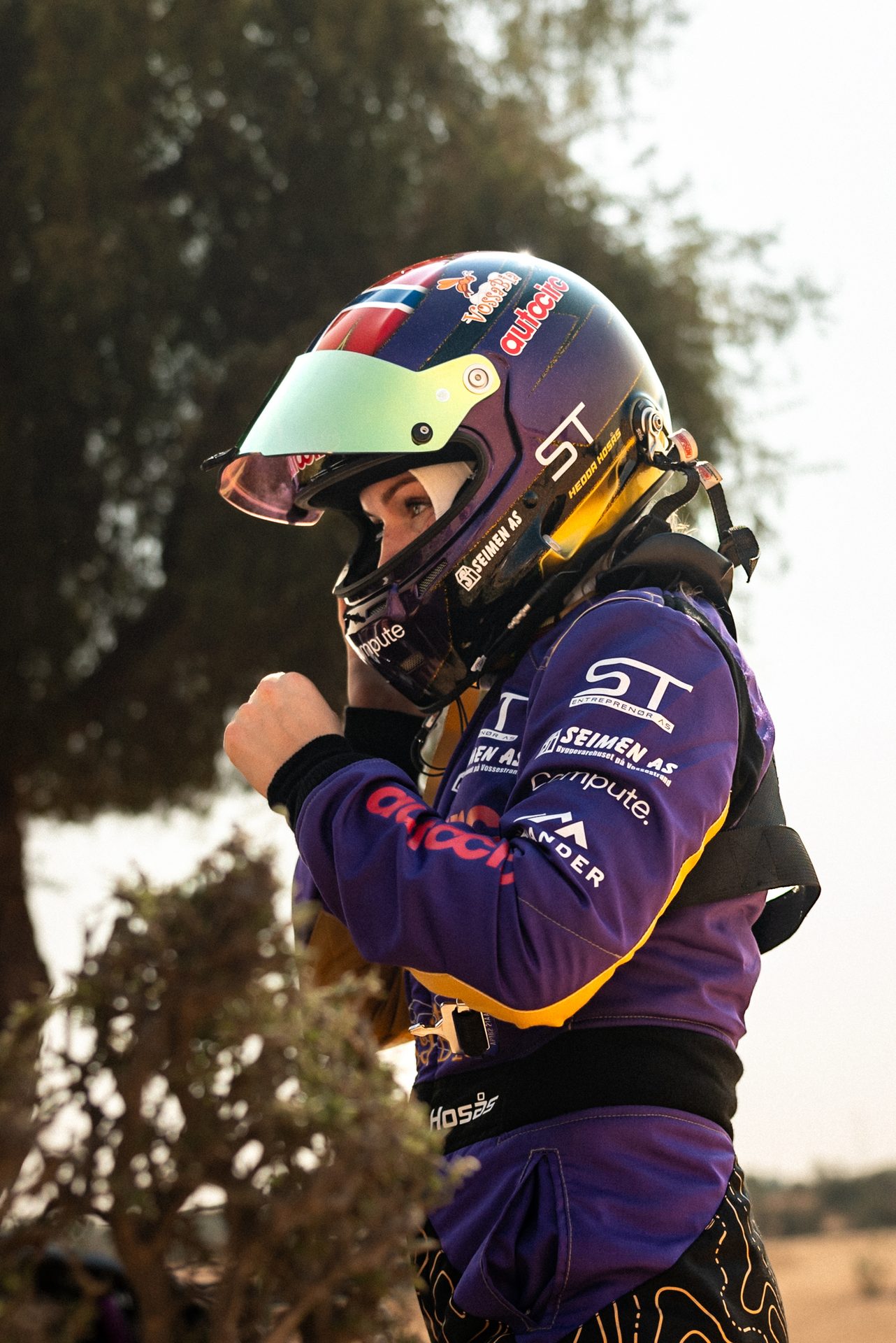 Racer Hedda Hosås in a purple suit and helmet with a green visor, fists clenched, looking focused.