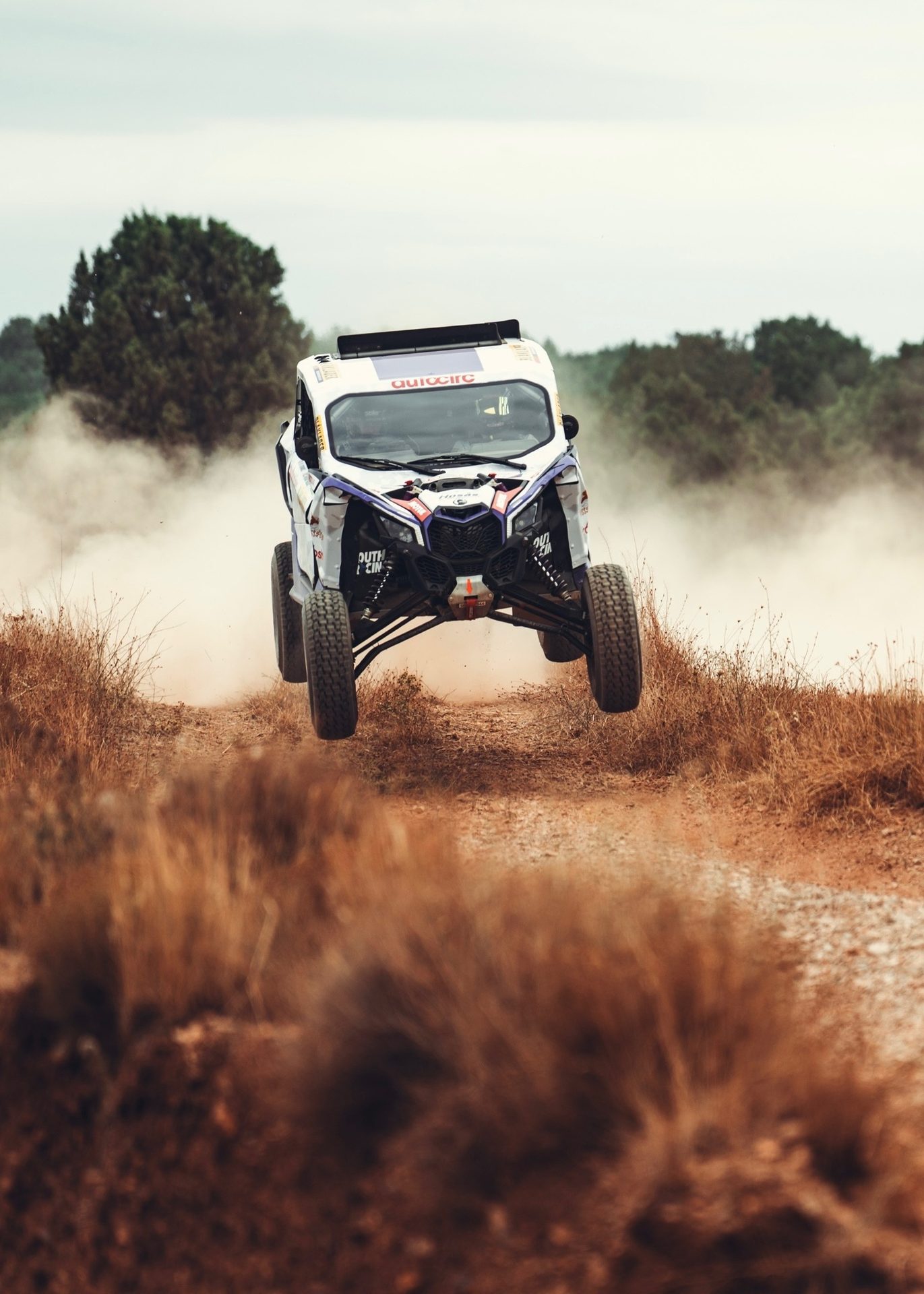 Off-road buggy jumping on a dusty track, surrounded by dry grass and trees.
