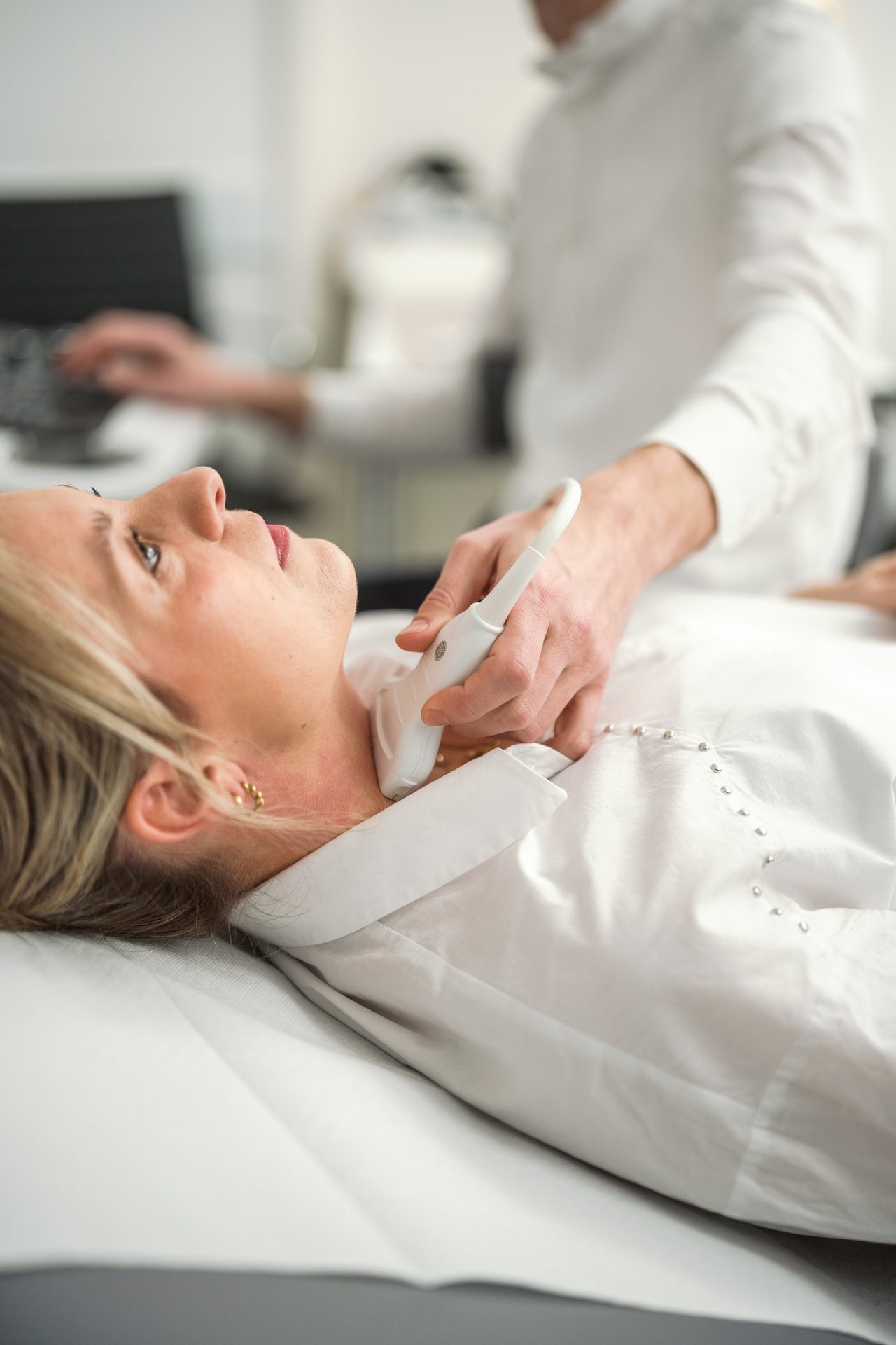 A doctor performs an ultrasound scan on a woman's neck in a clinical environment.