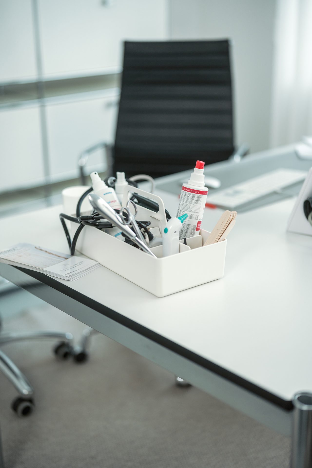 Medical tools and supplies in a white organizer box on a desk in an office setting.