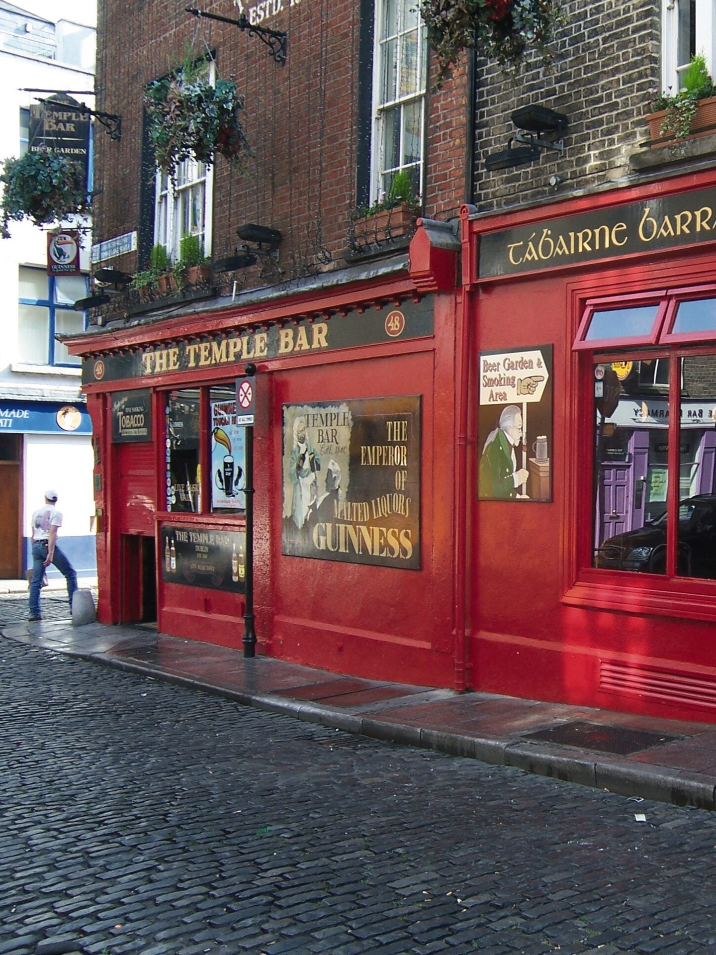 An iconic red pub called The Temple Bar with Guinness signs and a cobblestone street in Dublin, Ireland.