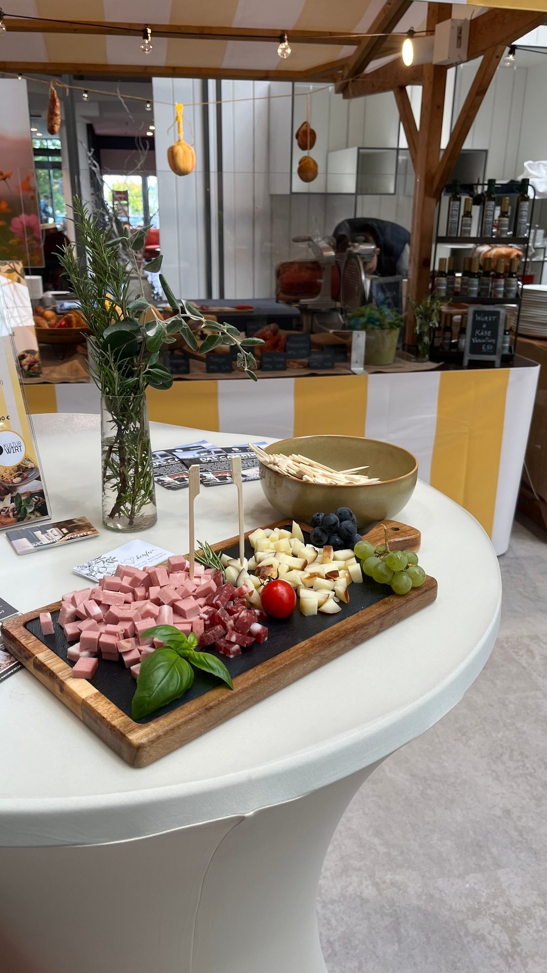 A charcuterie board with cheese, meats, grapes, and basil on a white table in a marketplace.