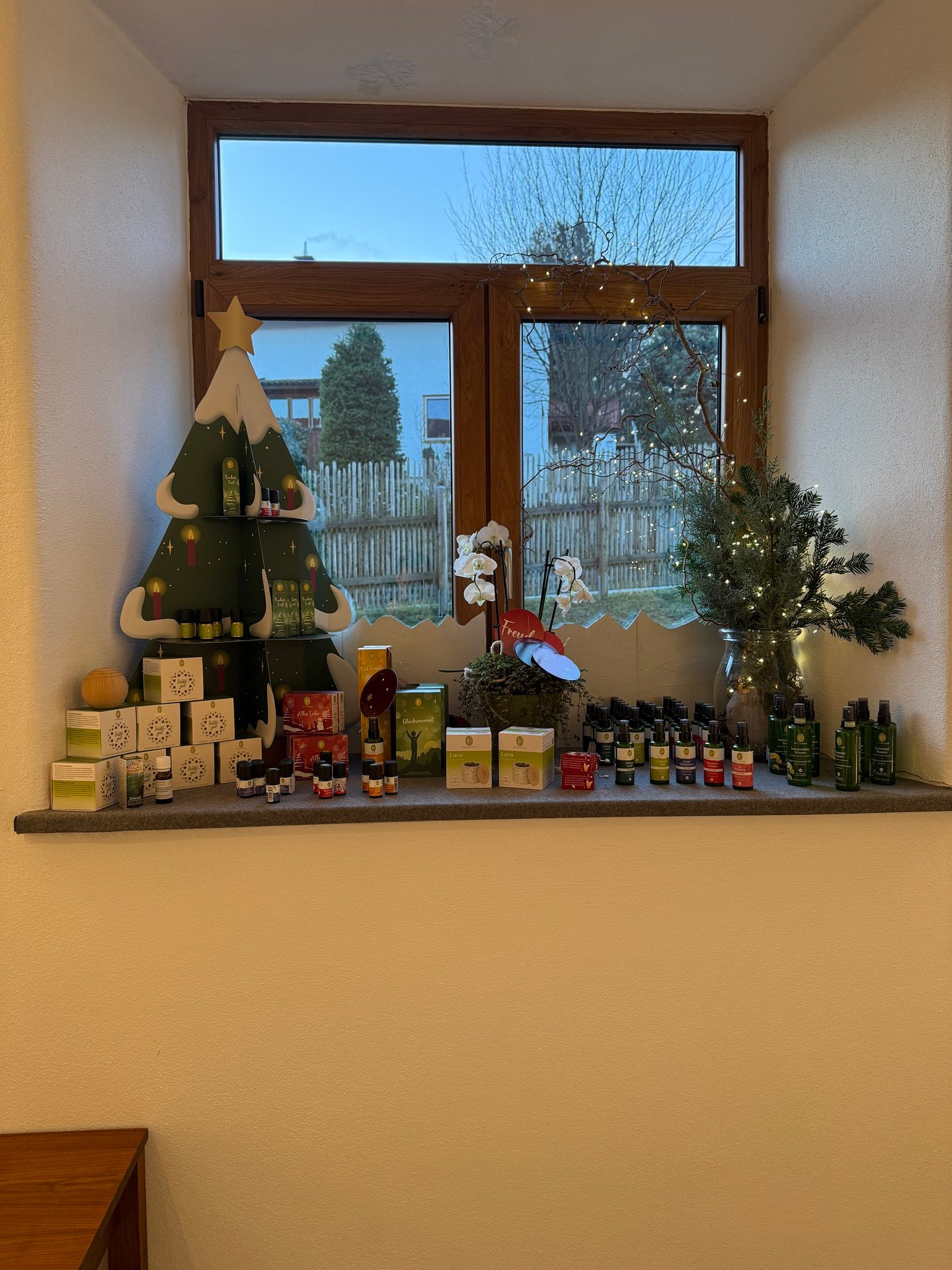 Festive window sill display with essential oil products, a decorative tree, and winter greenery.