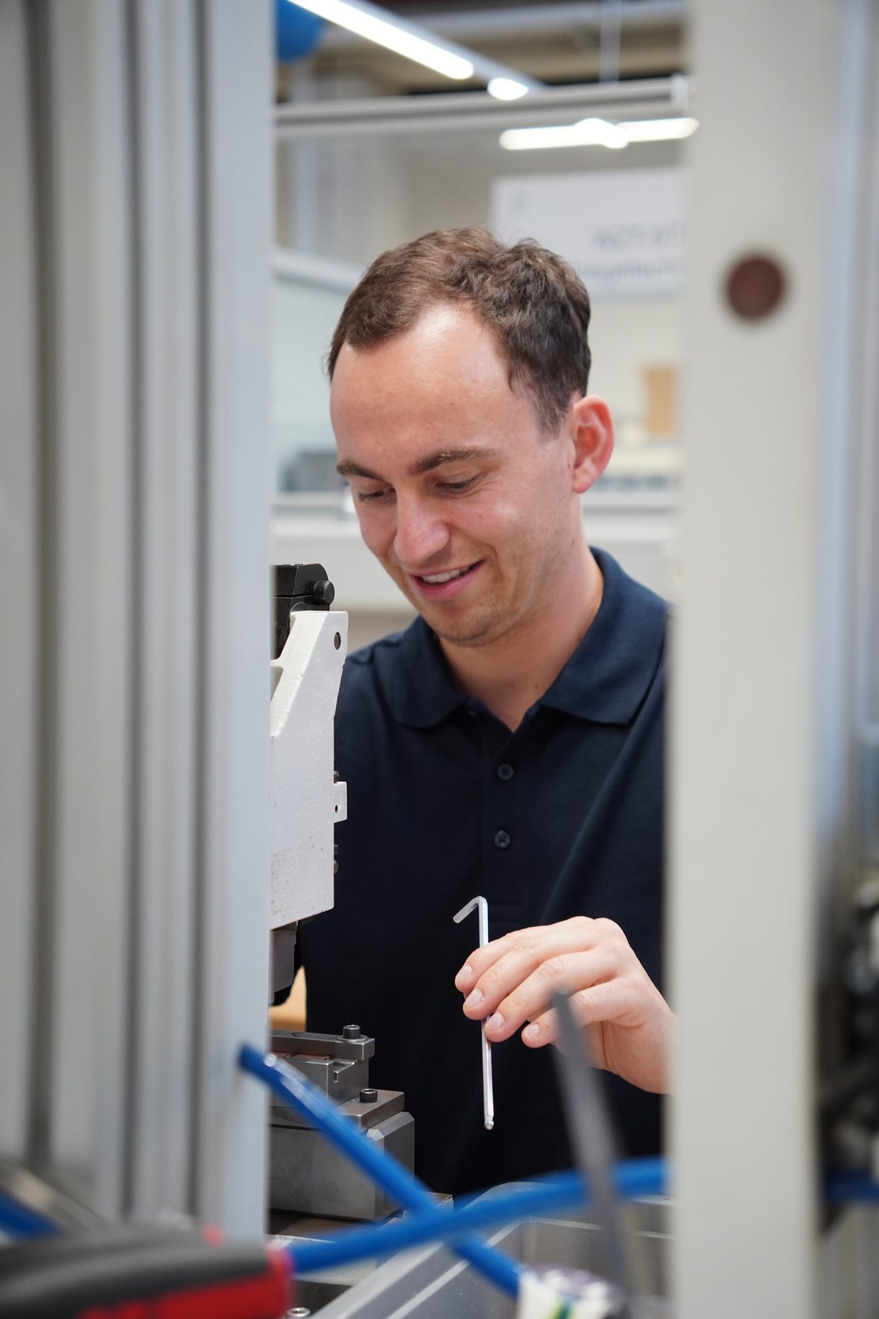 Young man smiling while working with an Allen wrench on a machine in a workshop.