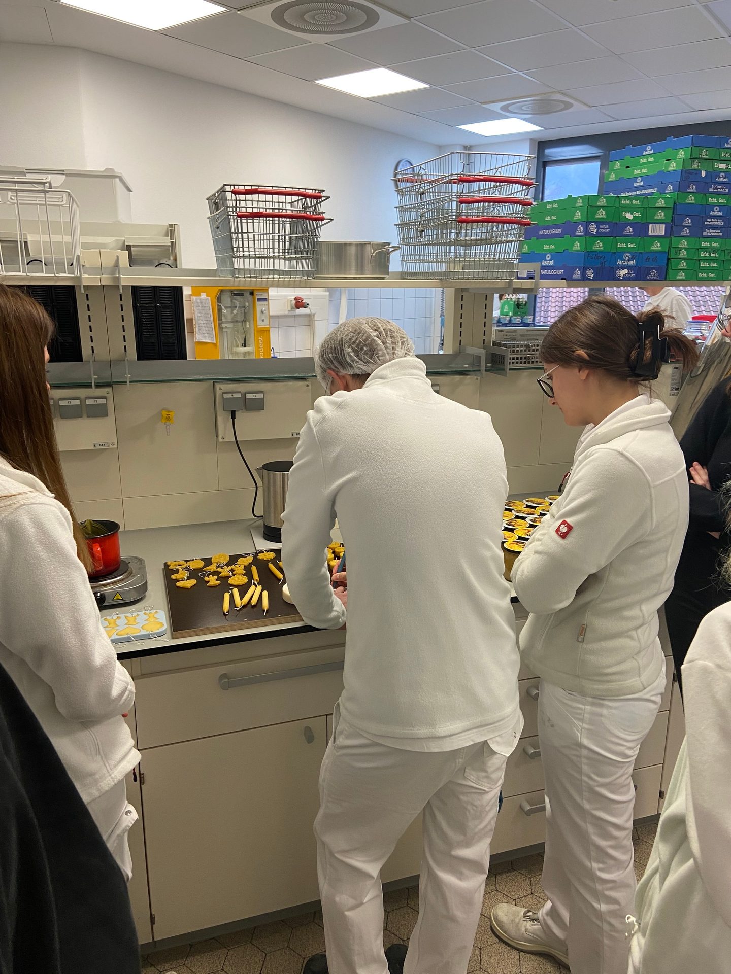 People in white uniforms preparing yellow pastries on a baking sheet in a professional kitchen setting.