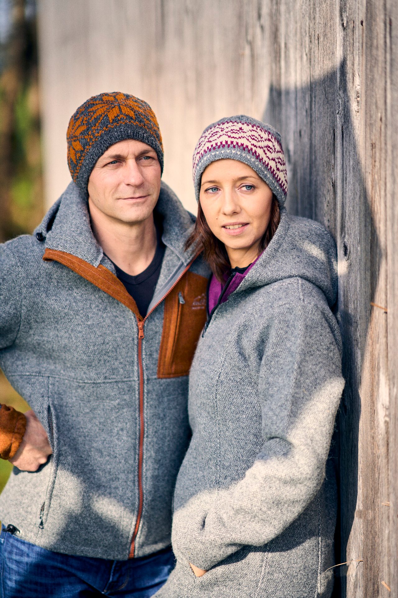 Man and woman wearing gray wool jackets and patterned knitted hats outdoors.
