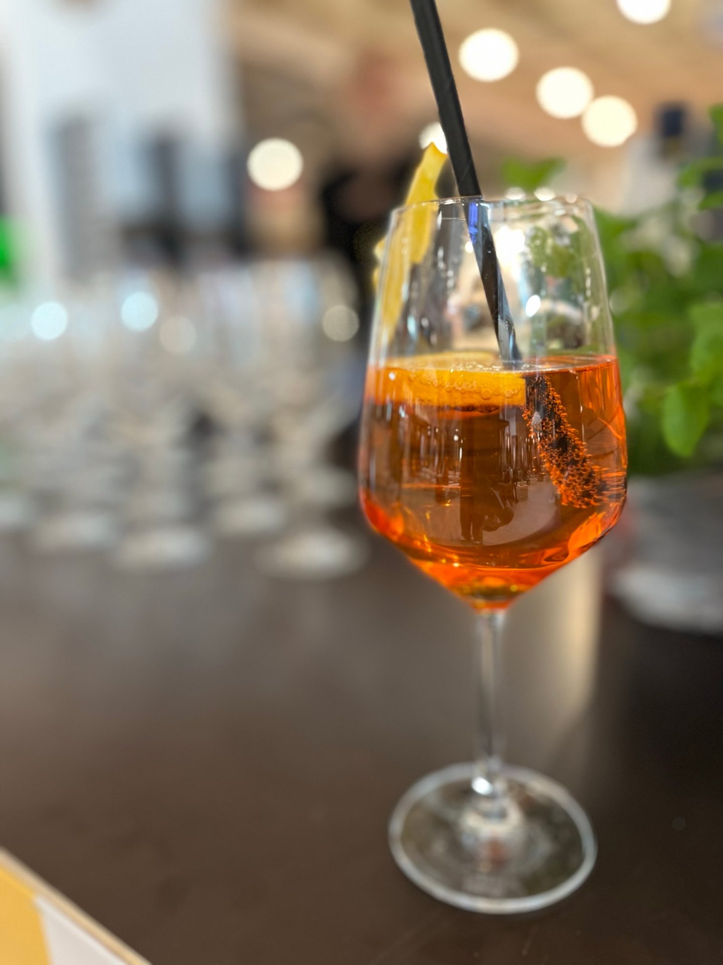 Orange drink in a stemmed glass with a straw and lemon slice, blurred background.