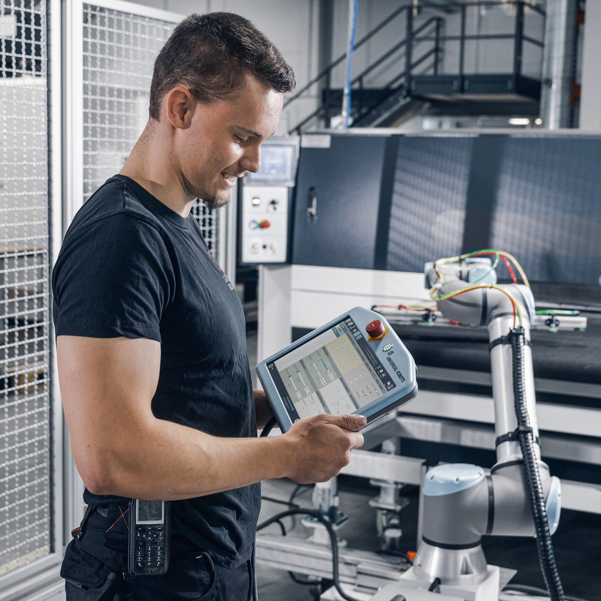 Man programs a robot using a tablet in a factory.