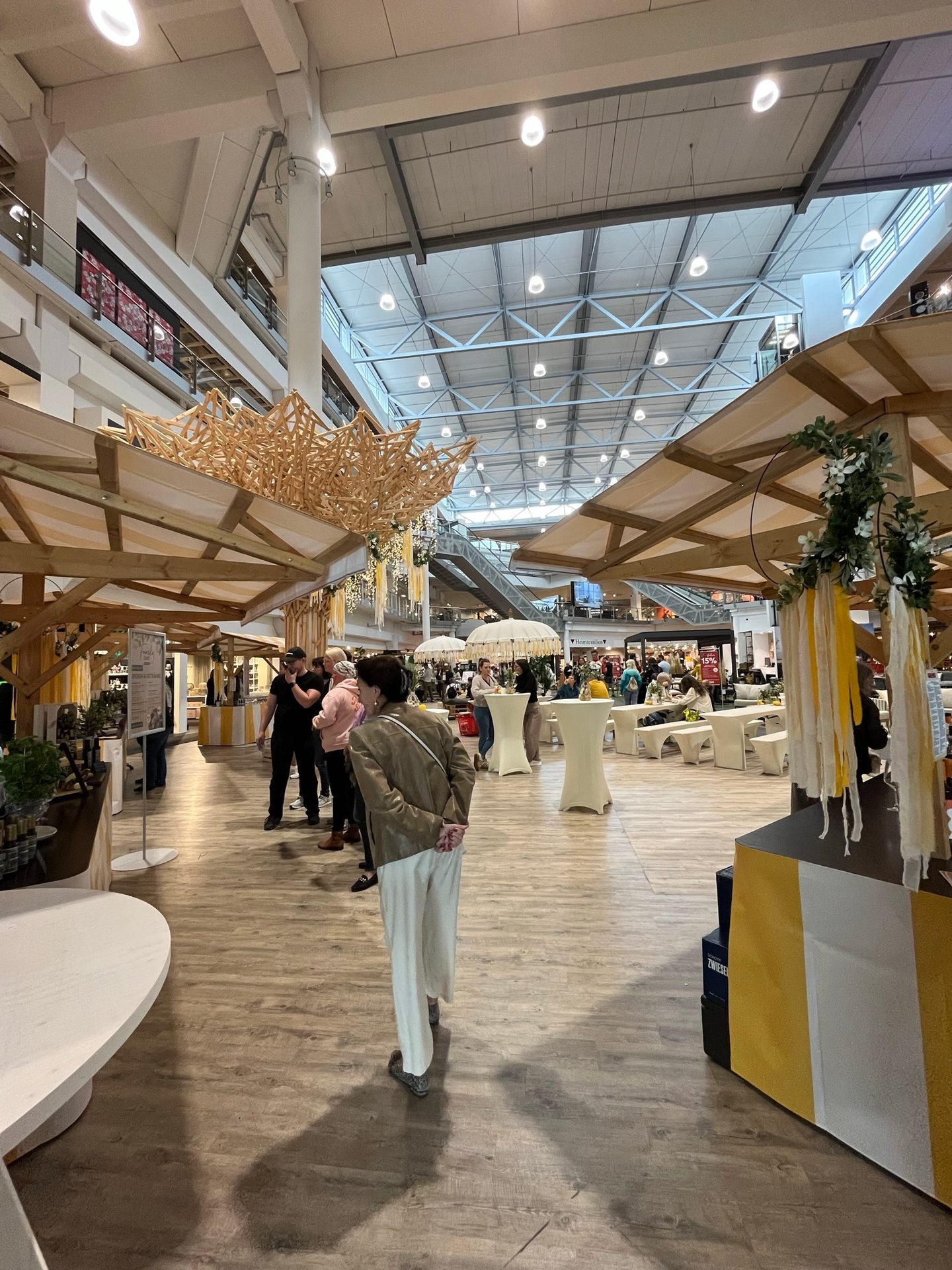 A bustling indoor market with people, wooden stalls, and a bright, high ceiling.