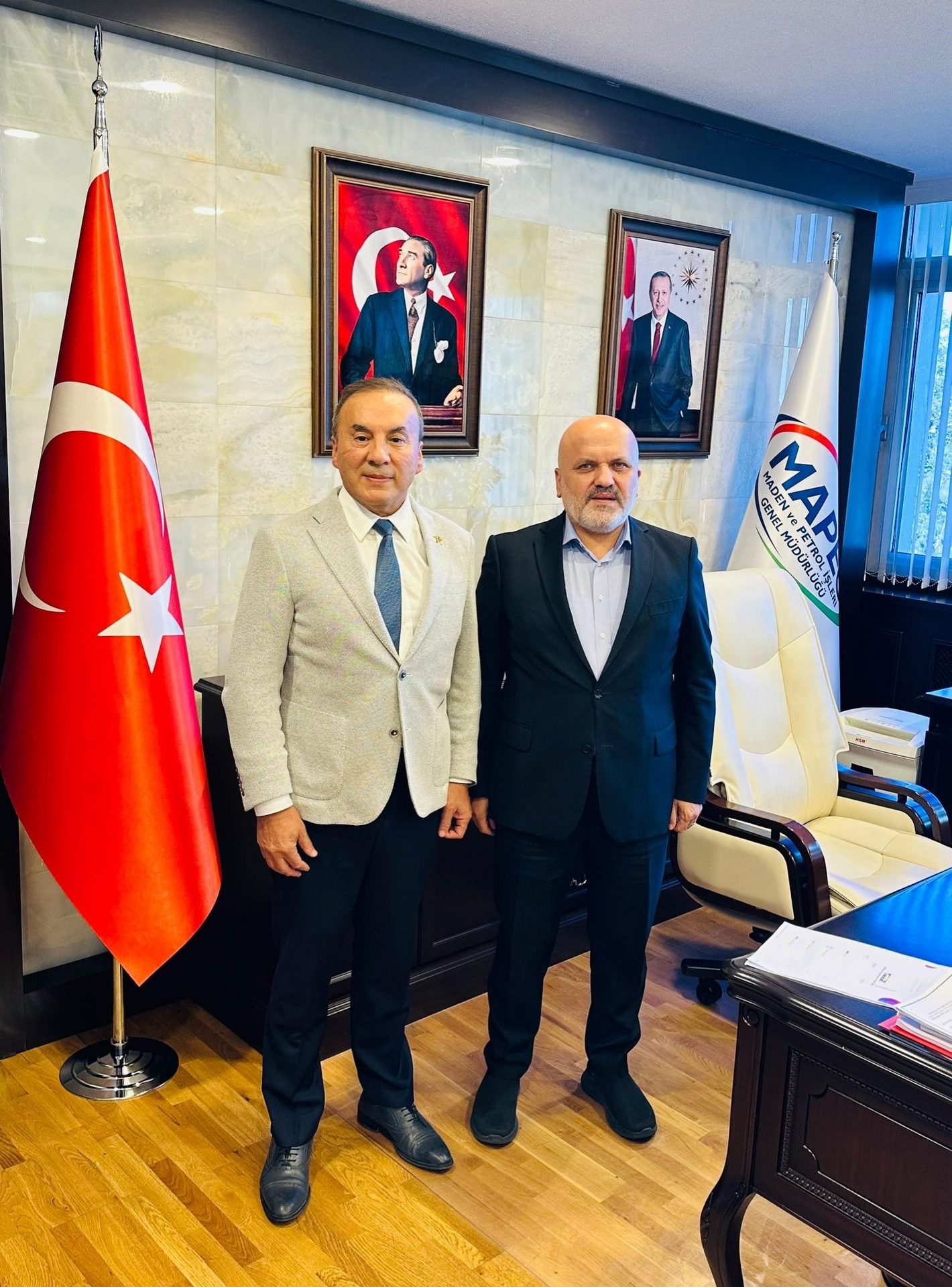 Two men in suits stand in an office next to the Turkish flag and portraits of Atatürk and Erdoğan.
