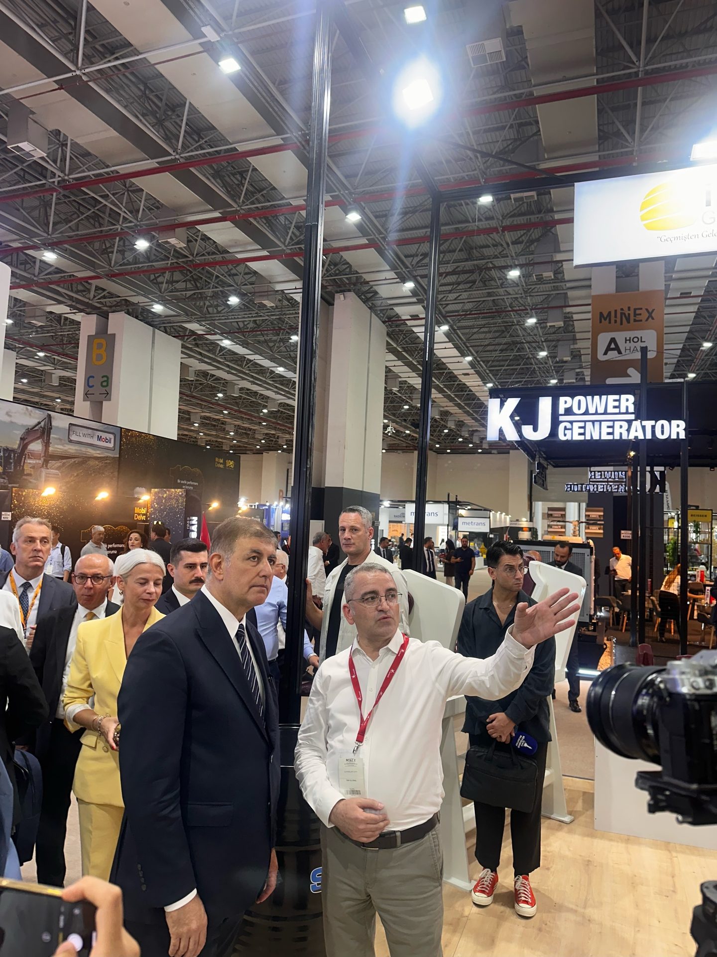 A man gestures to a group of people at a trade show, near a "KJ POWER GENERATOR" sign.