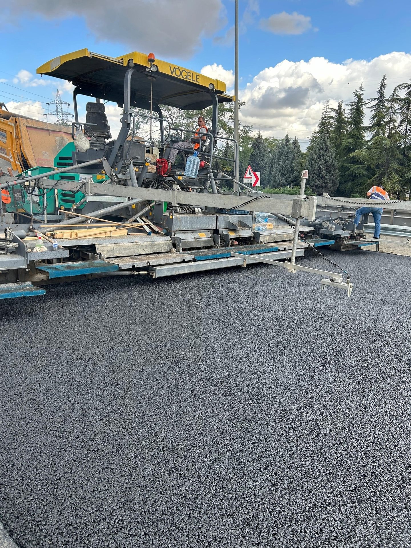 Vögele asphalt paver laying fresh blacktop on a road, with workers.