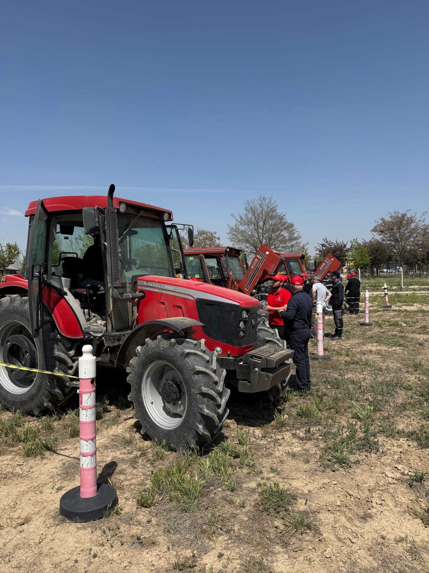Red Tumosan 8100 tractor and people gathered around other red tractors outdoors.