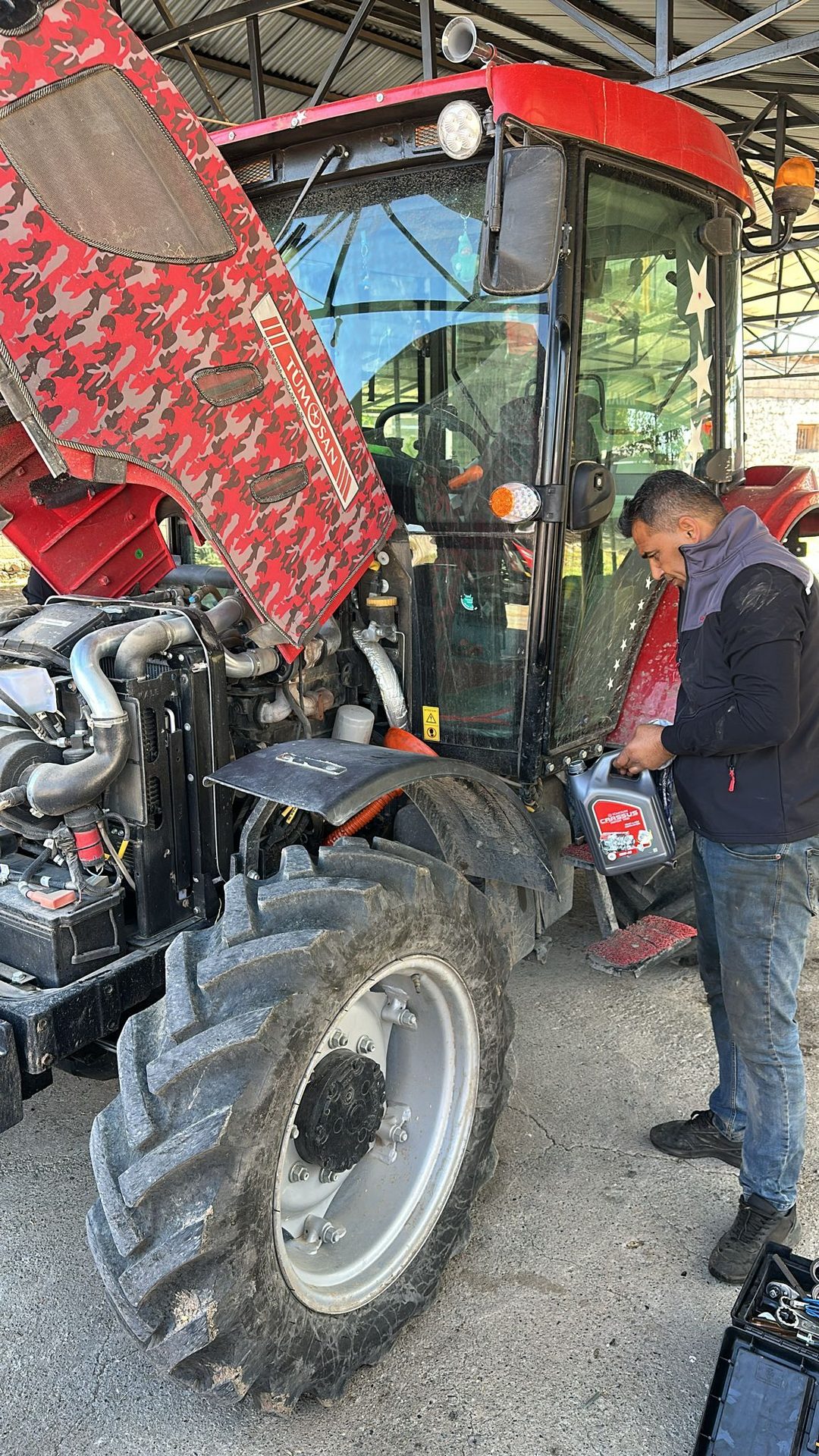 Man pouring oil into a red TÜMOSAN tractor with its hood open.