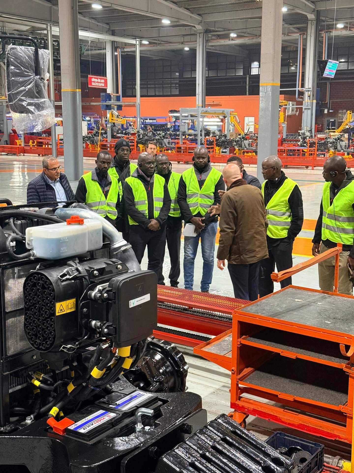 Men in safety vests observe industrial machinery in a factory setting.