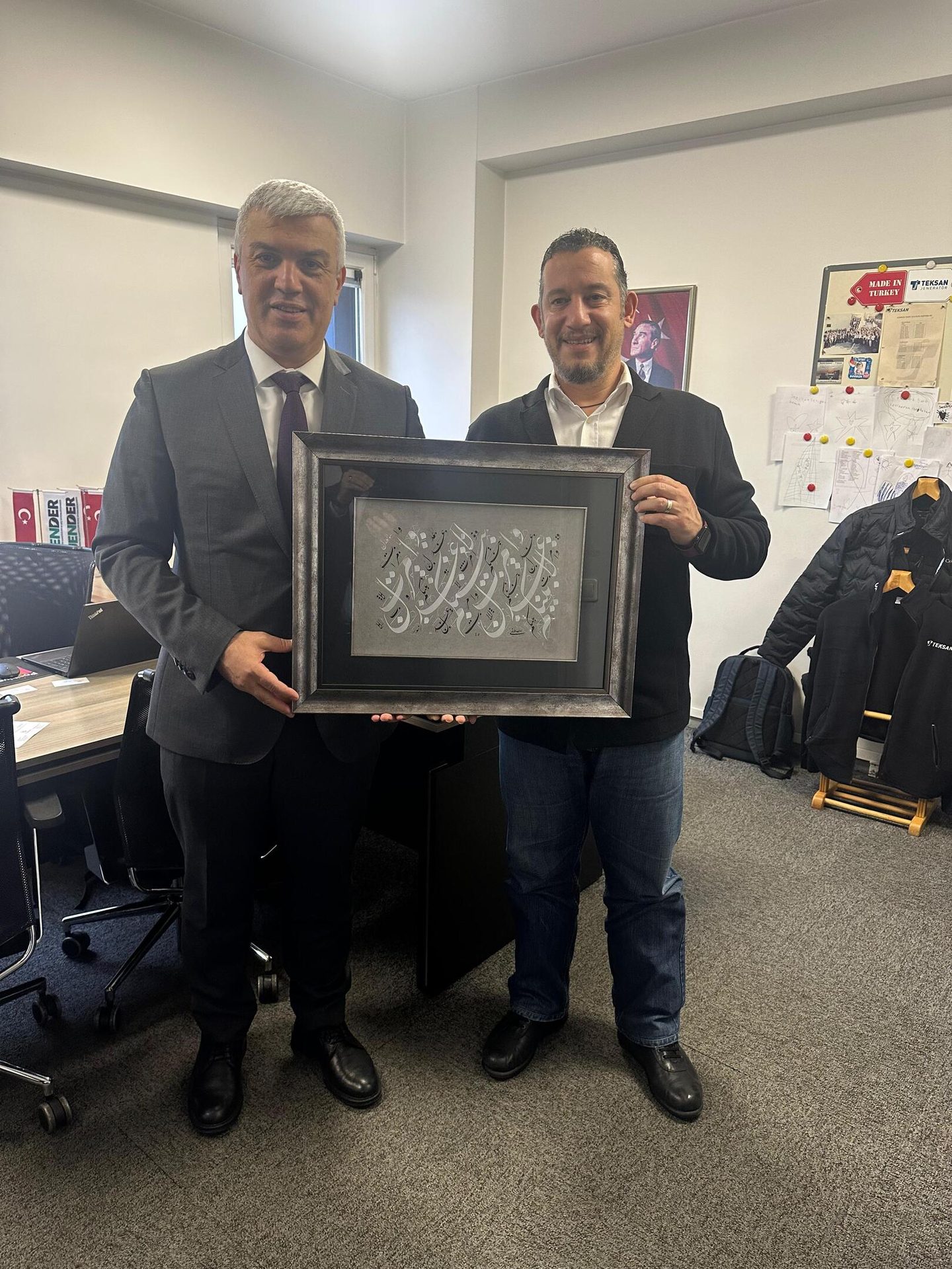 Two men in an office holding a framed calligraphy artwork.