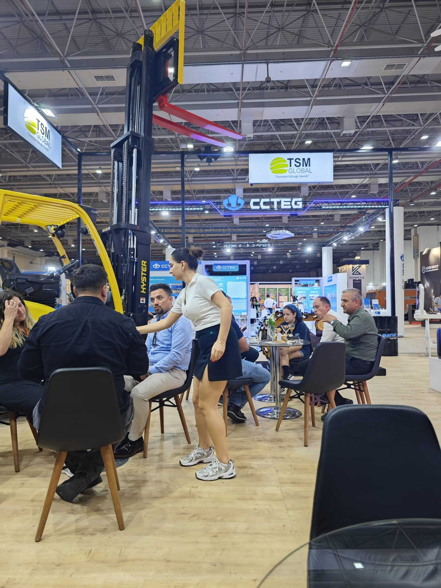 People at an indoor trade show with a forklift, company logos like TSM GLOBAL, CCTEG, and Hyster.