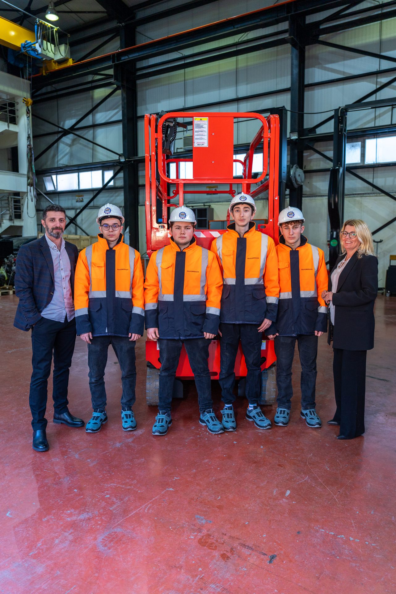 Four students in safety gear and two adults standing in an industrial facility with machinery.