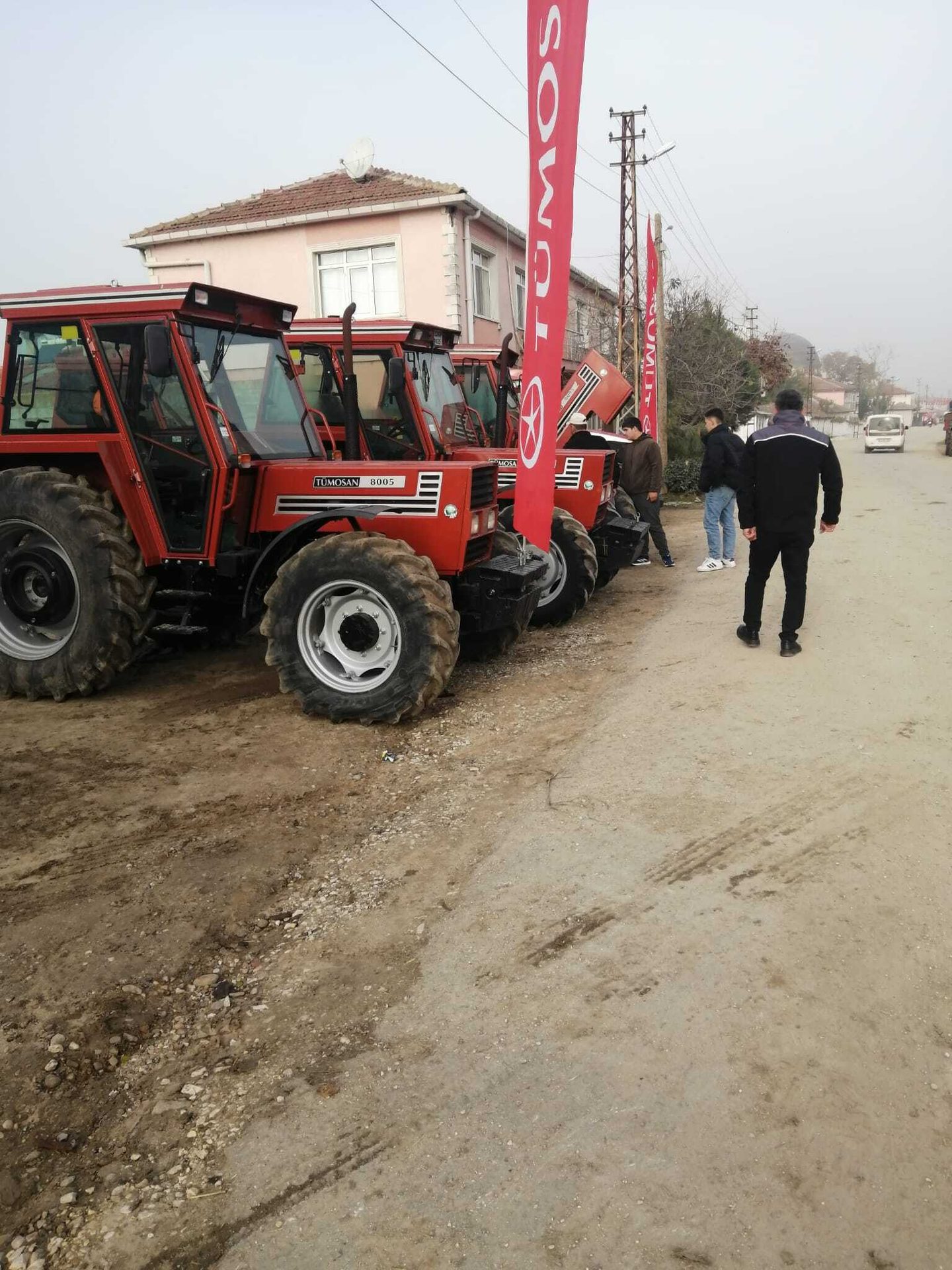 Red TÜMOSAN tractors parked on a dirt road with people around them.