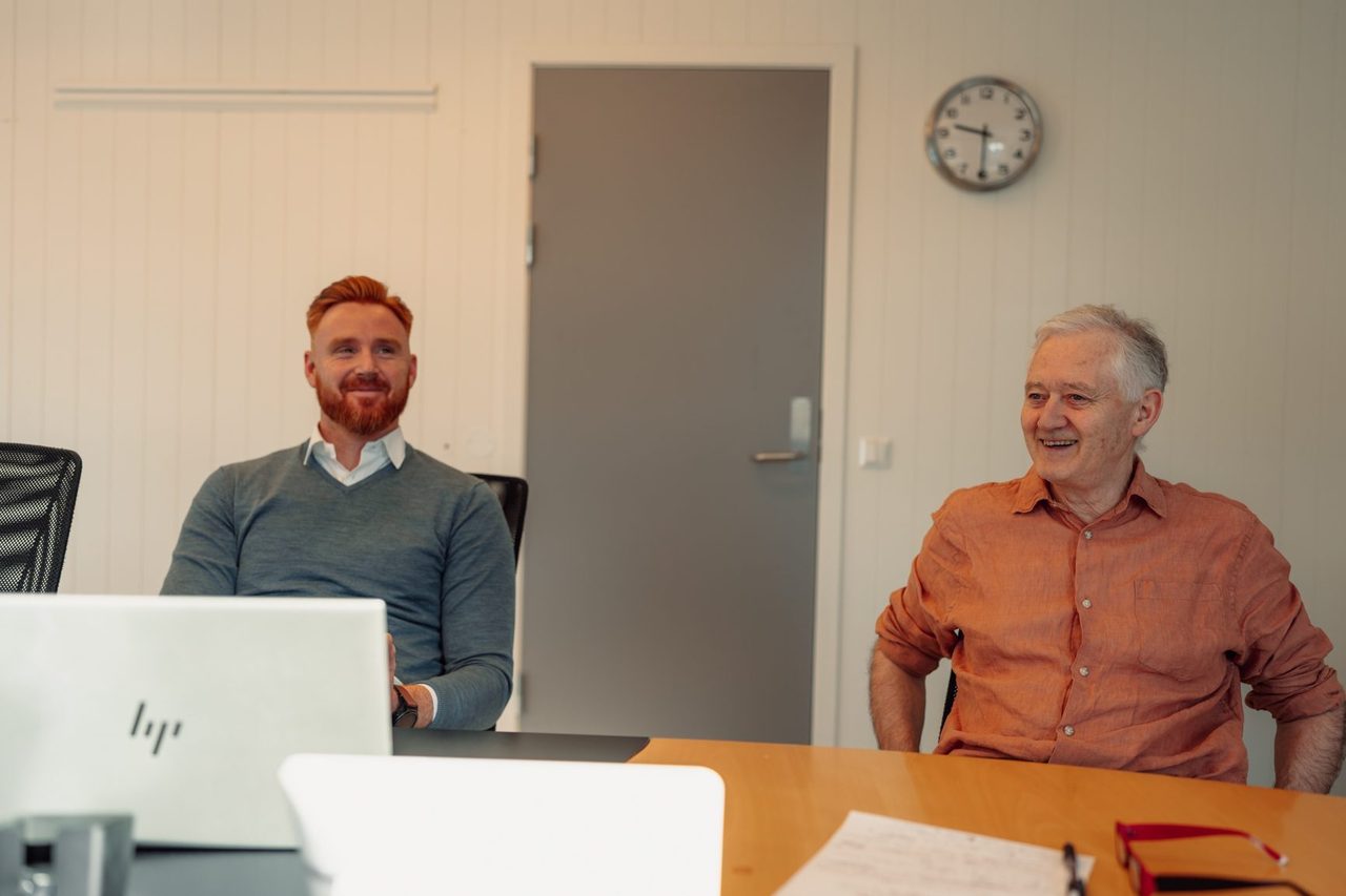 Interior design, White-collar worker, Furniture, Table, Shirt, Smile, Desk, Sitting, Wrist, Room