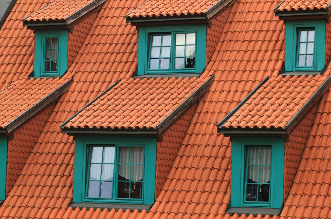 Close-up of an orange tiled roof with green framed dormer windows, creating a colorful architectural contrast.. Pixabay: https://www.pexels.com/@pixabay