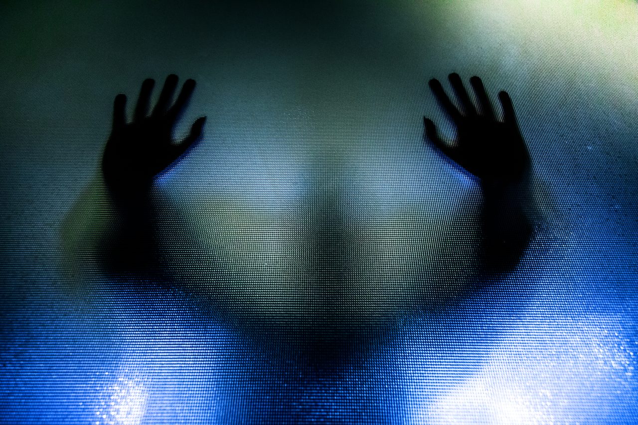 Silhouette of depressed abused woman with hands pressed against glass