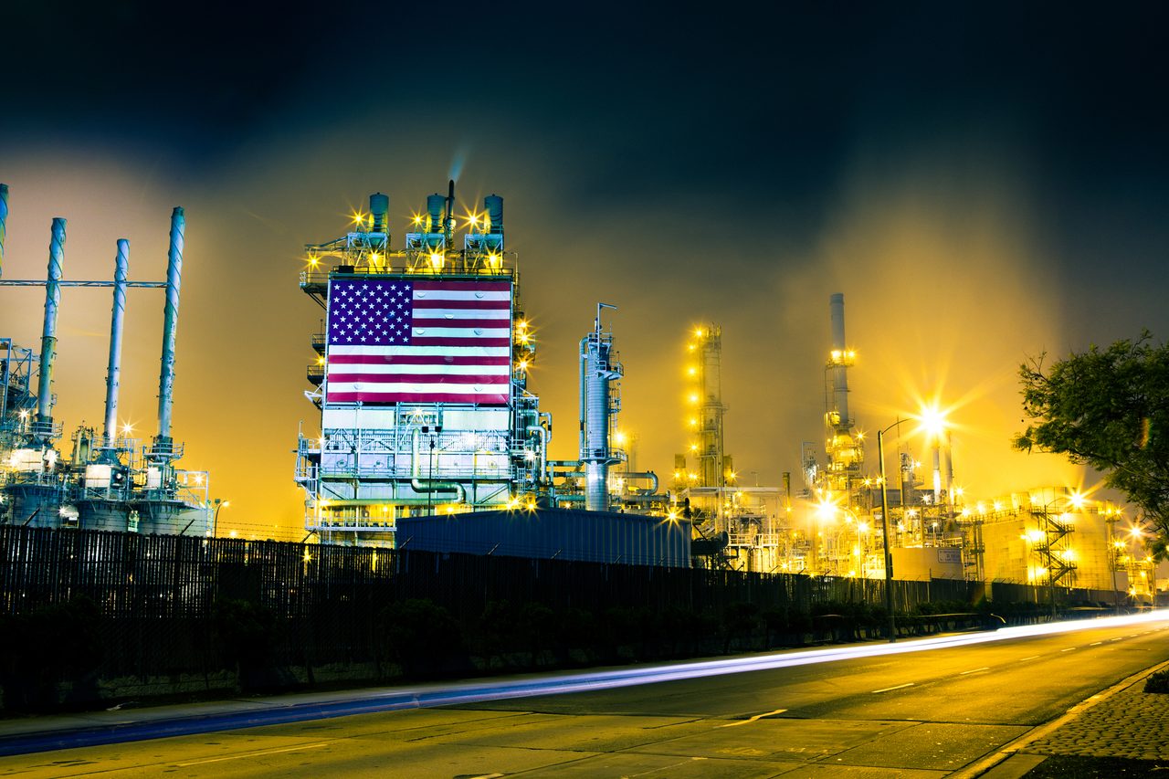 Headlights from cars streak across the frame in front of a large oil refinery complex in Los Angeles, CA