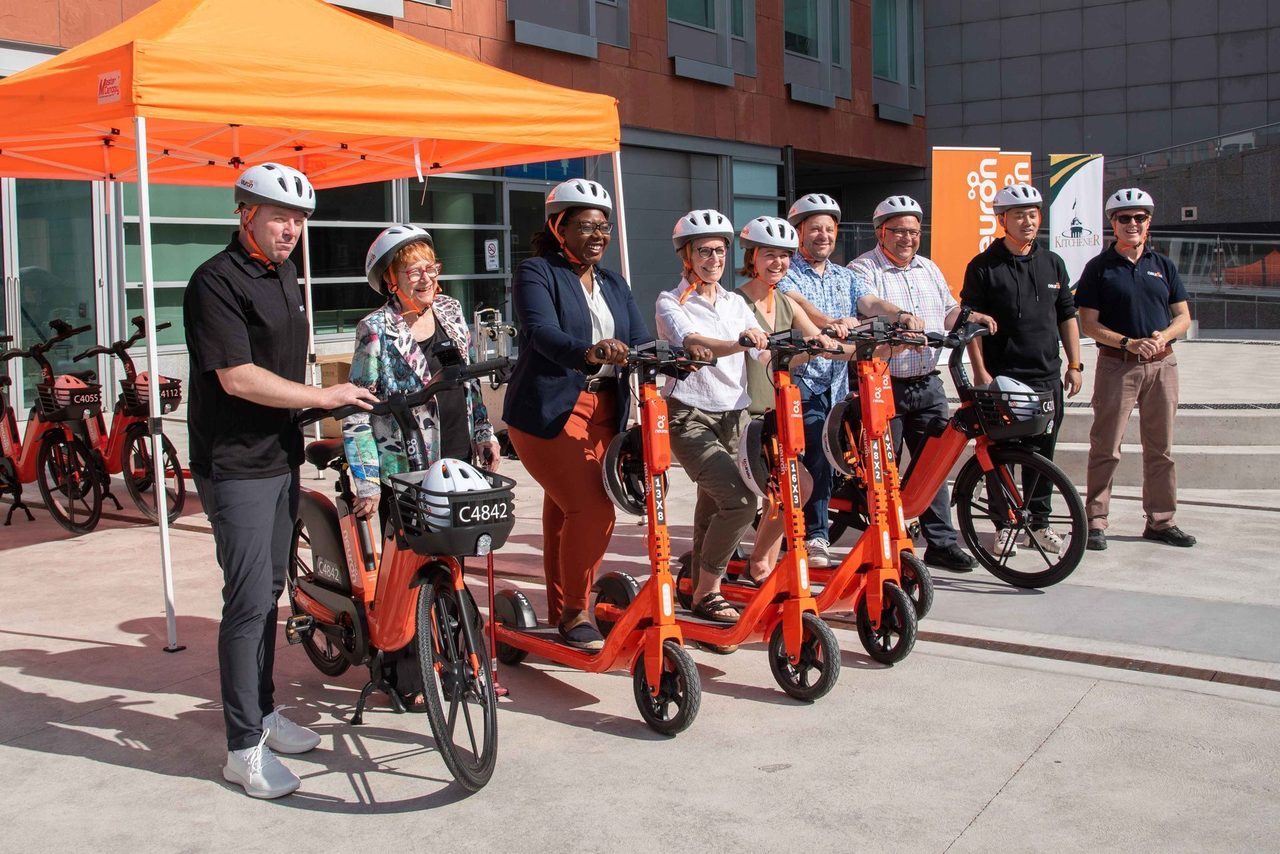 Region of Waterloo council members and other members of the public pose with Neuron scooters and bikes.