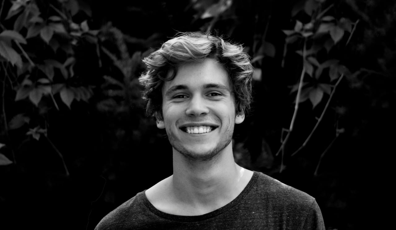 A black and white portrait of a young man smiling outdoors with natural background.. Stefan Stefancik: https://www.pexels.com/@stefanstefancik