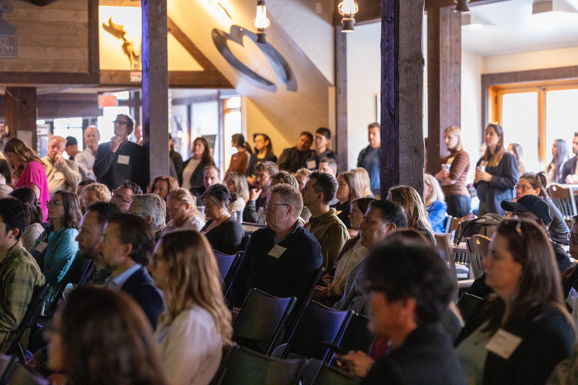 Attendees at an indoor event, some seated, some standing, looking forward.