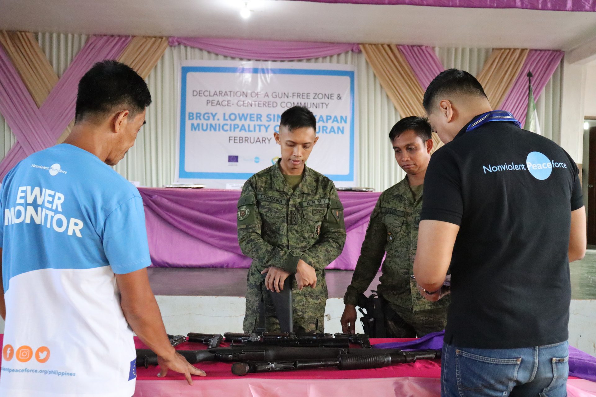 Military and peace monitors inspect guns at a "gun-free zone" declaration event.