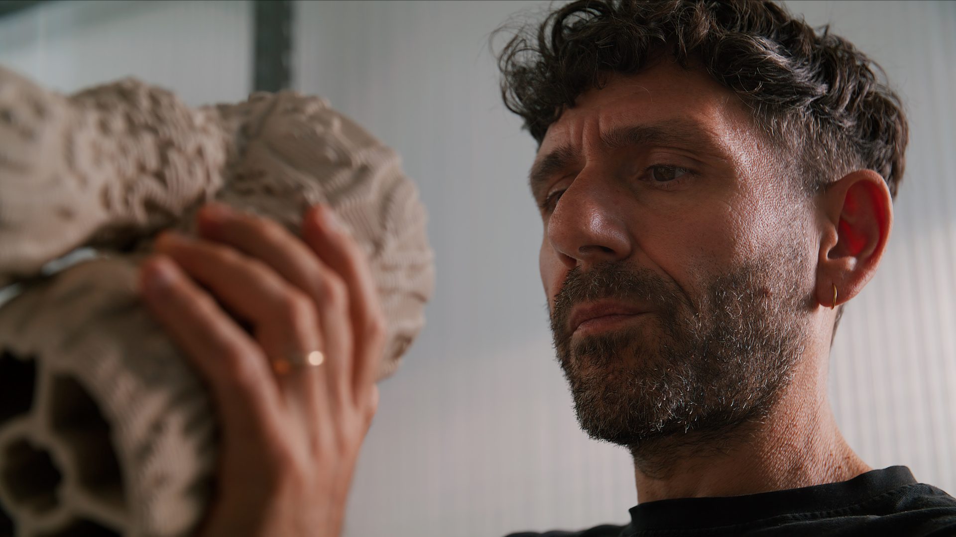 Man with beard and curly hair intently examines an intricate, light-colored object he holds.