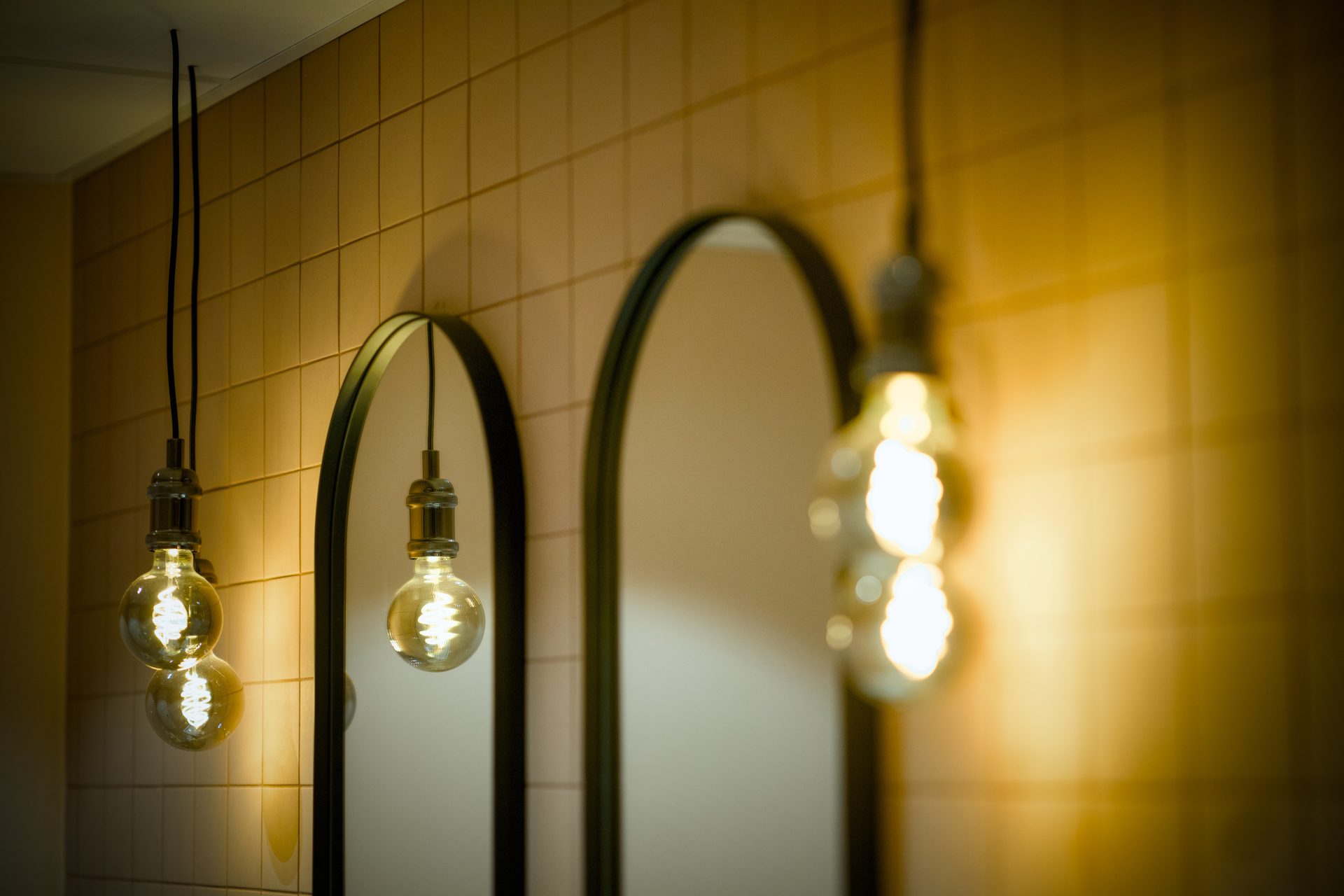 Glowing Edison bulbs and an arched mirror against a warm tiled wall.