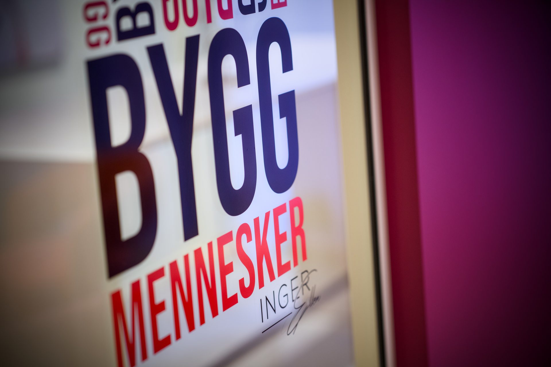 A sign displaying "BYGG MENNESKER" in bold blue and red letters, with "INGER" and a signature.