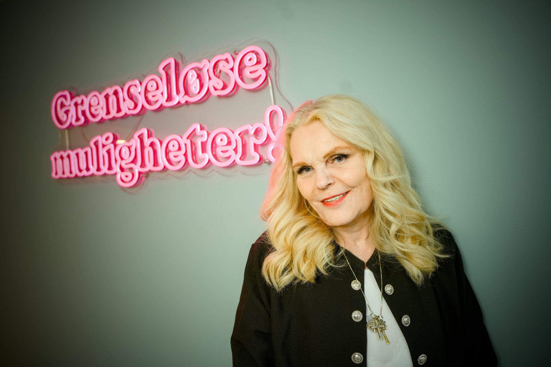 Smiling blonde woman next to a pink neon sign reading "Boundless possibilities!".