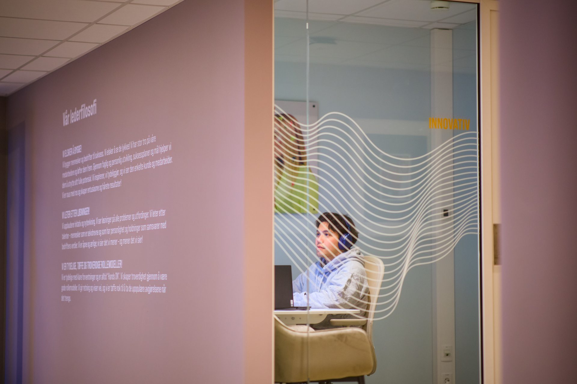 Person at laptop behind wavy glass with "INNOVATIV". Text about philosophy on a wall.