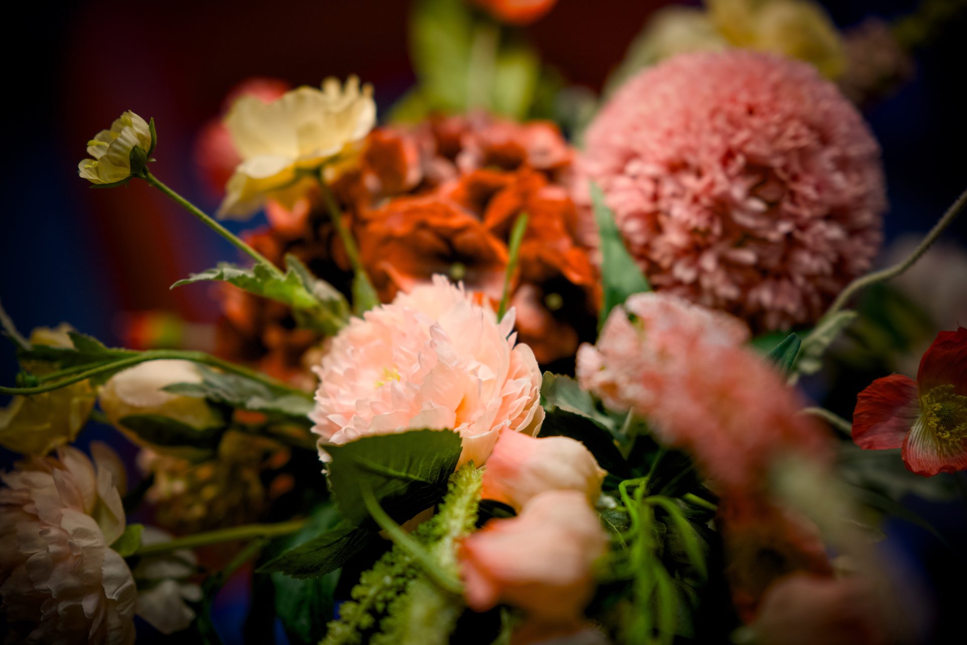 A vibrant, soft-focus bouquet with peach, red, and yellow flowers and green foliage.