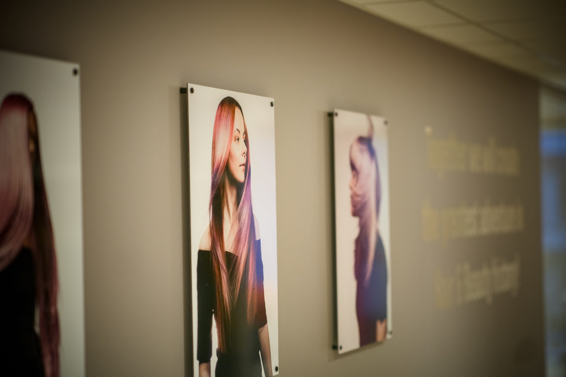 Wall with three portraits of women showcasing vibrant, styled hair and blurred text.