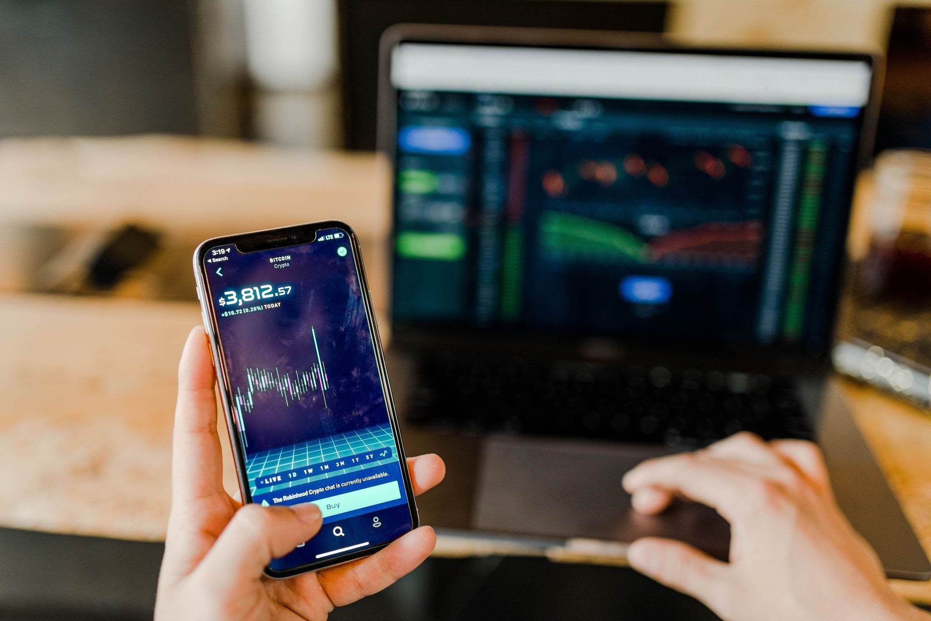 Hands view cryptocurrency data on a smartphone and financial charts on a laptop.
