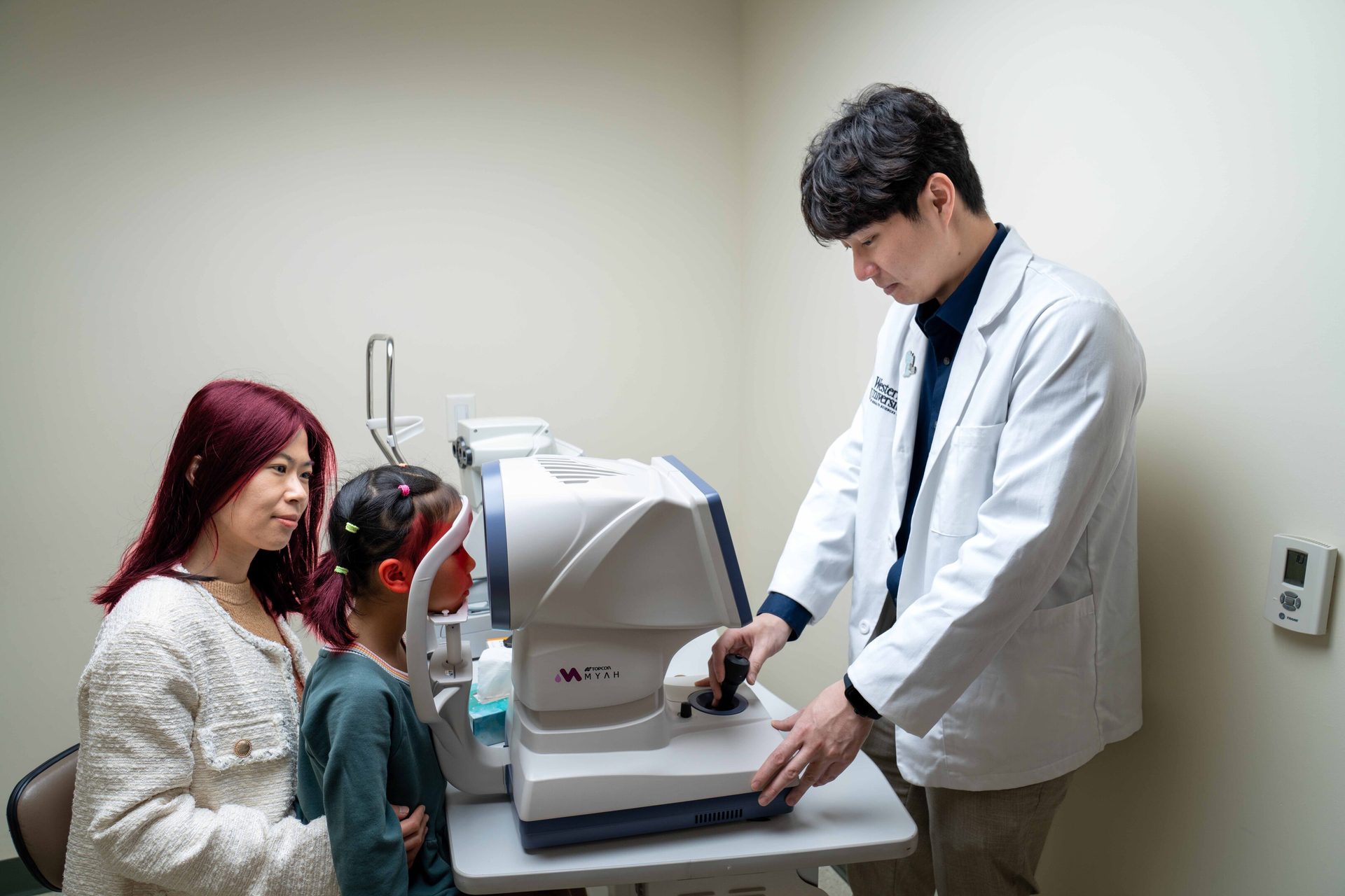 A doctor performs an eye exam on a child, with her mother's support.
