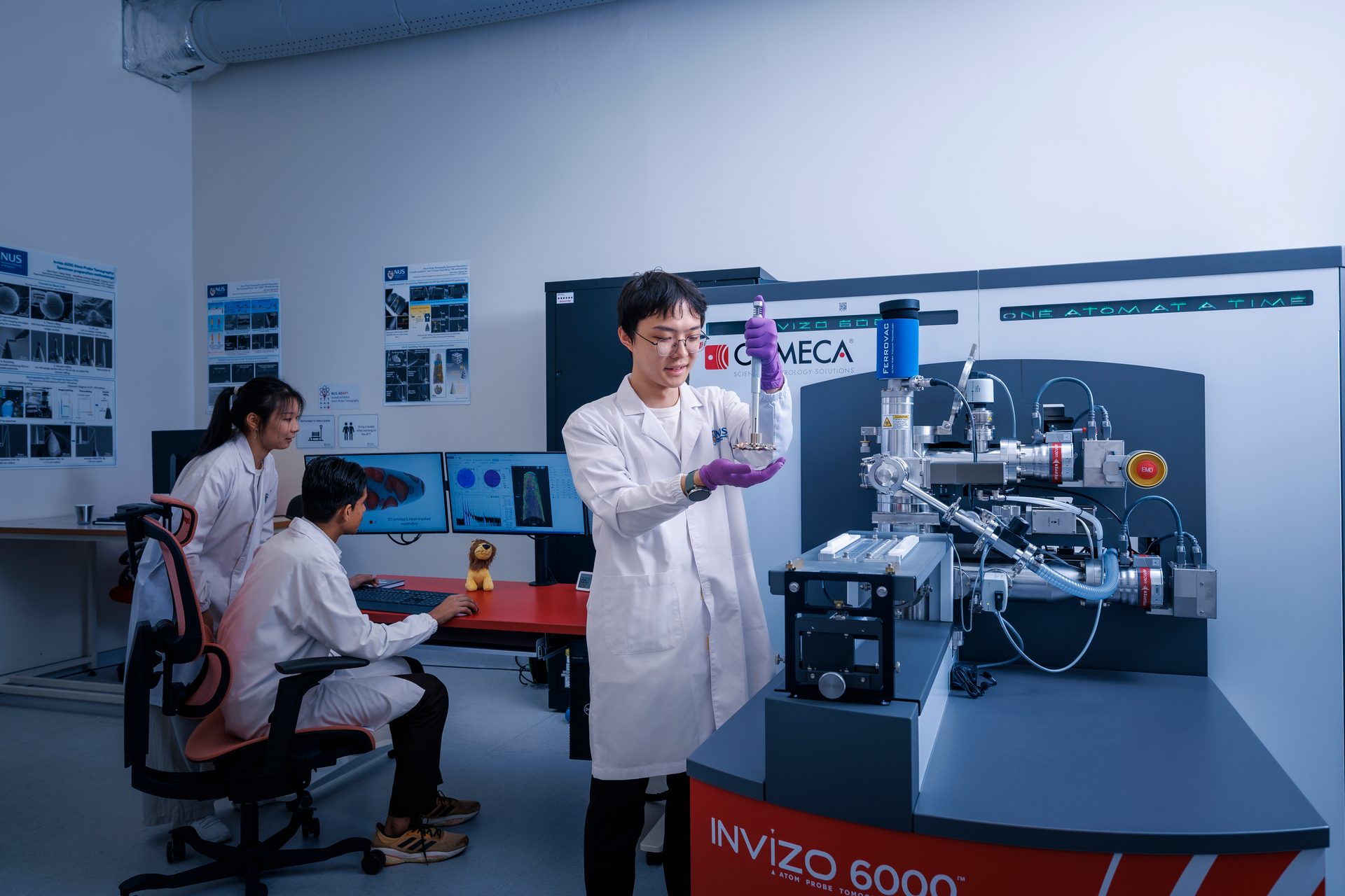 Three scientists in lab coats analyze data and operate an INVIZO 6000 atom probe tomograph.