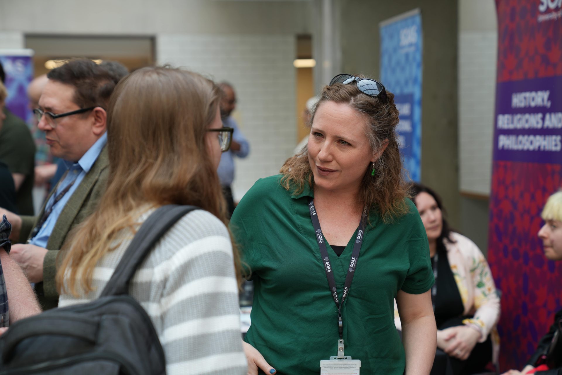 Two women talking; one in a green shirt with sunglasses, the other's back visible.