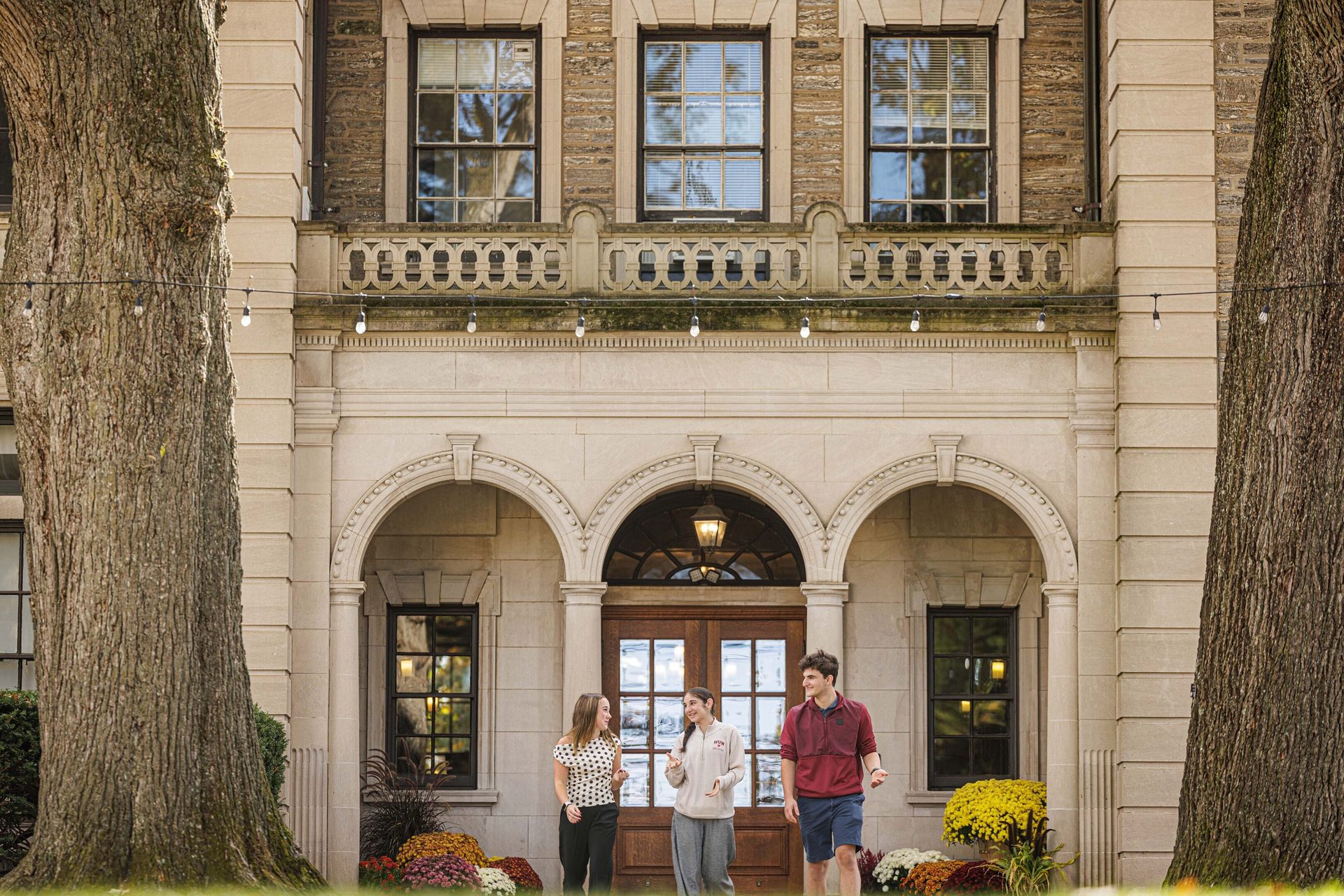 Three students walking and talking in front of a grand stone university building with arched entrances.