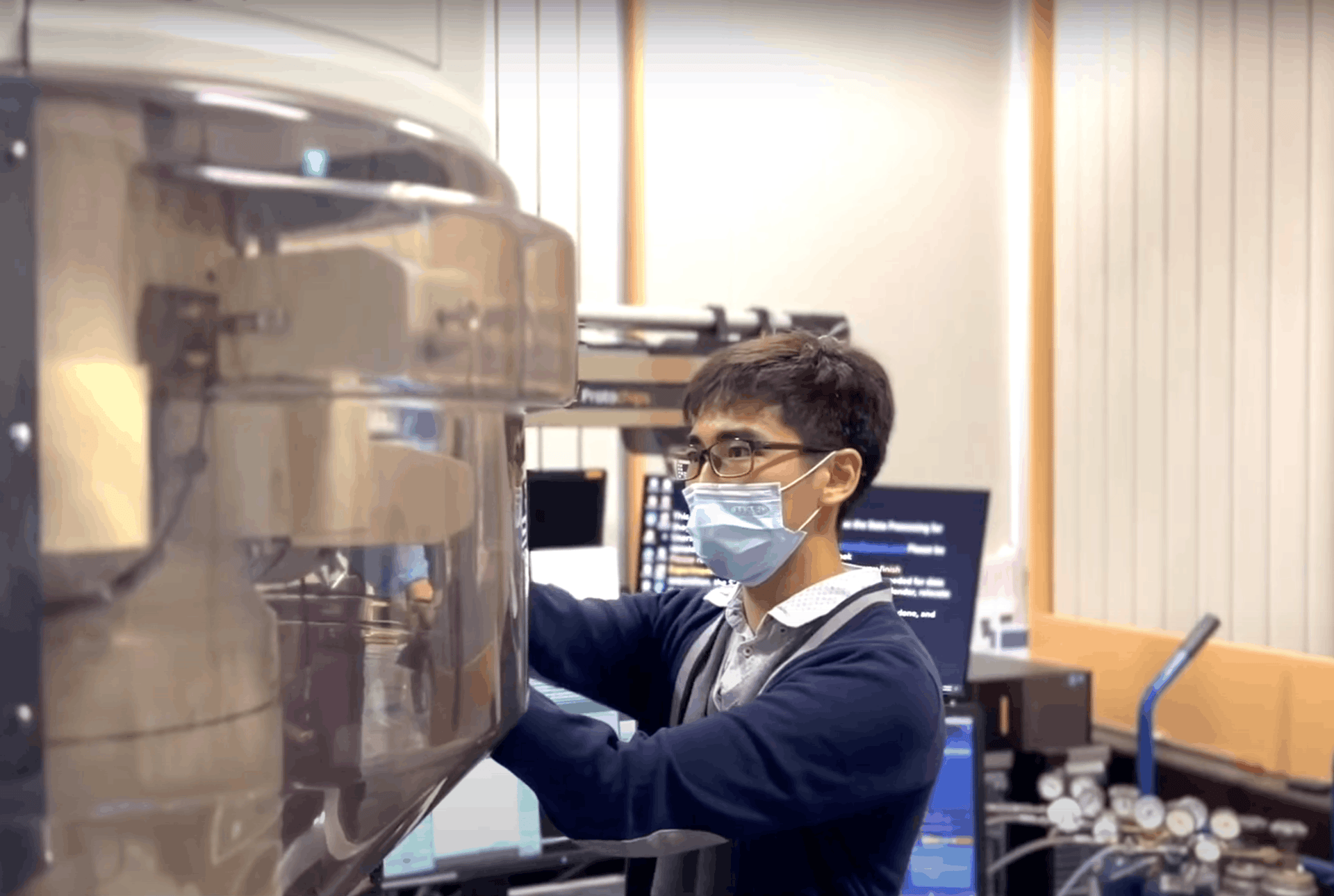 A researcher wearing a mask and glasses operates a large, complex piece of laboratory equipment.