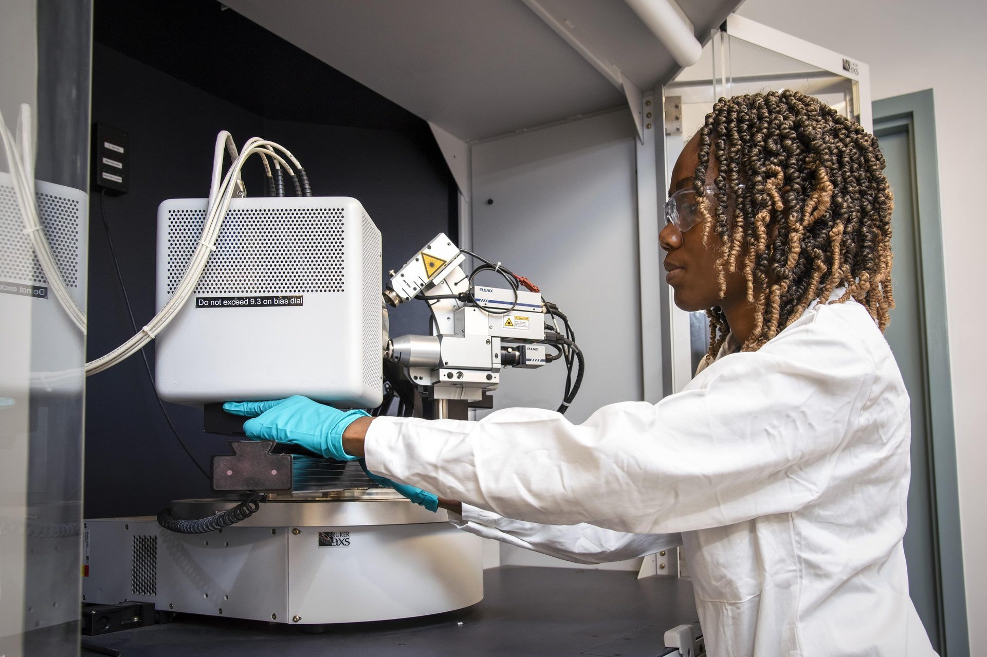 Scientist in safety glasses and lab coat operates a Bruker AXS machine.