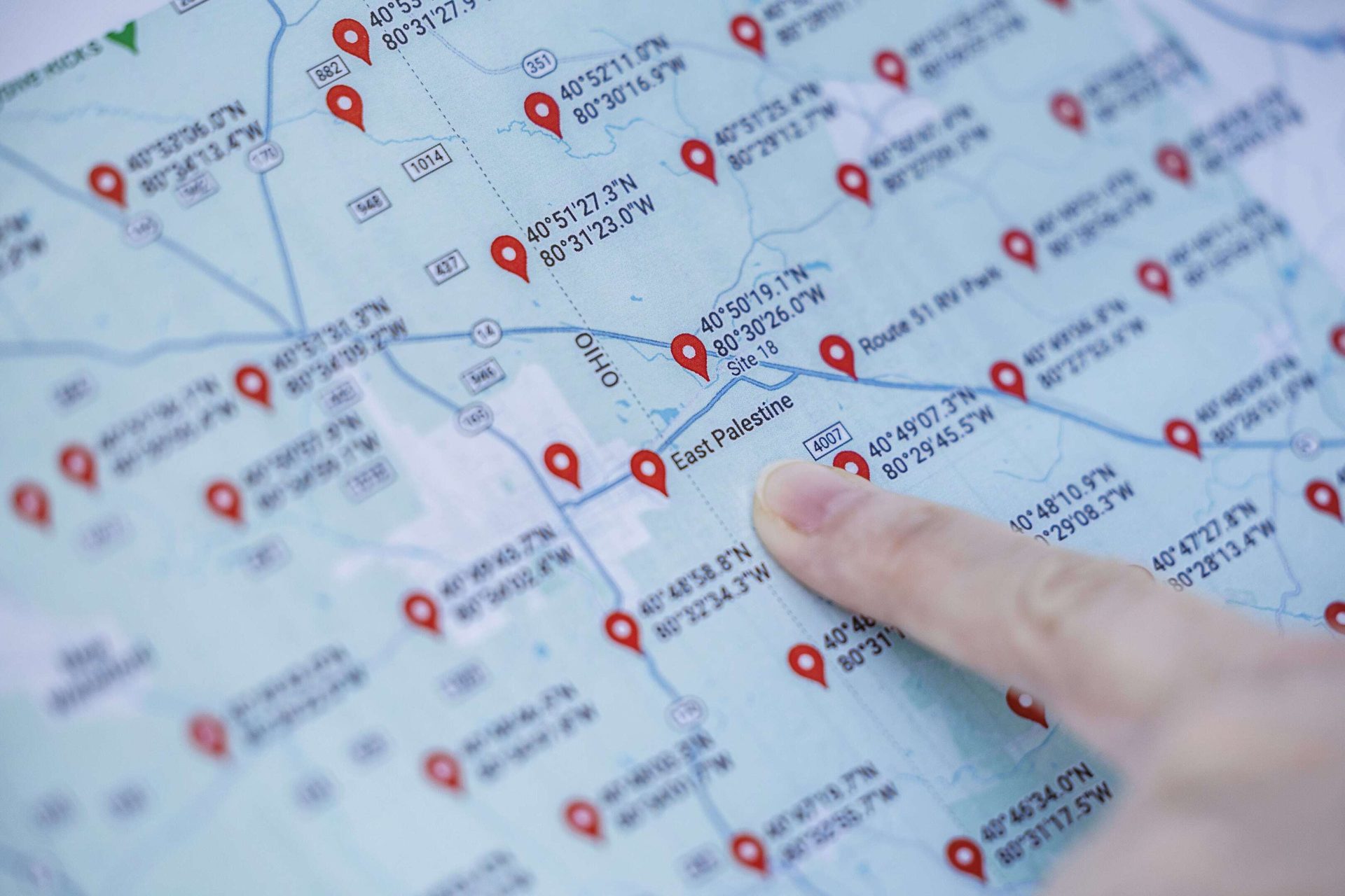 A finger points at 'East Palestine' on a map with red location pins and geographic coordinates.